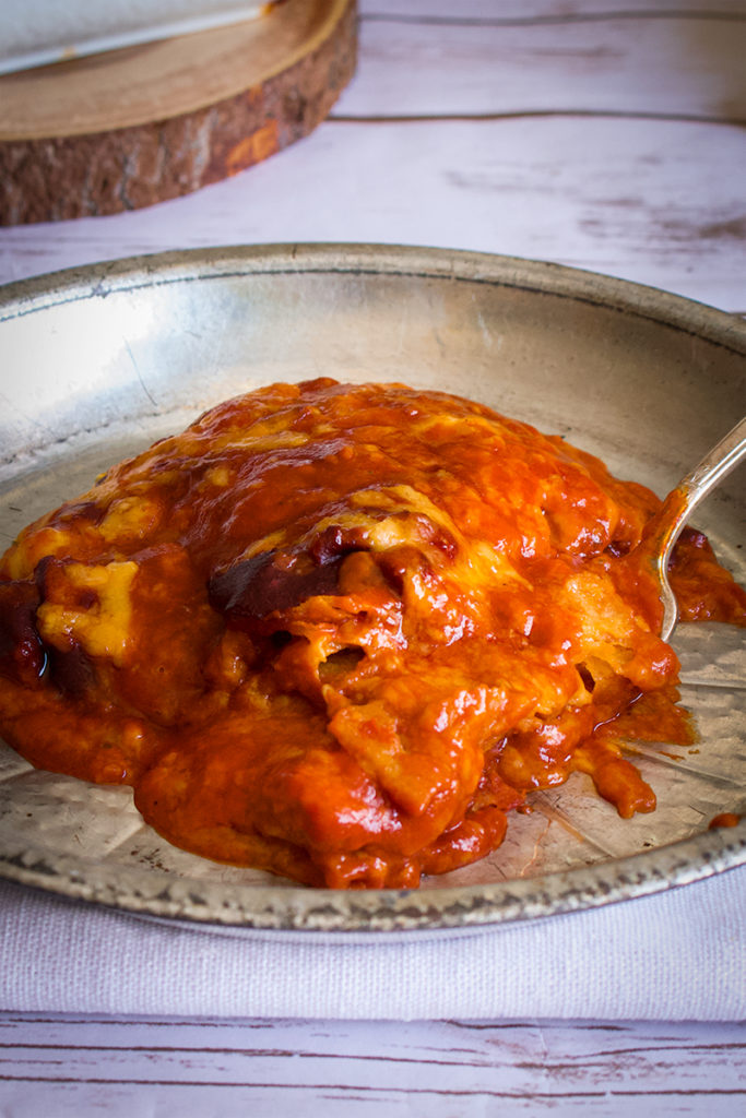 A tin plate filled with cheese enchiladas smothered in red chili enchilada sauce.