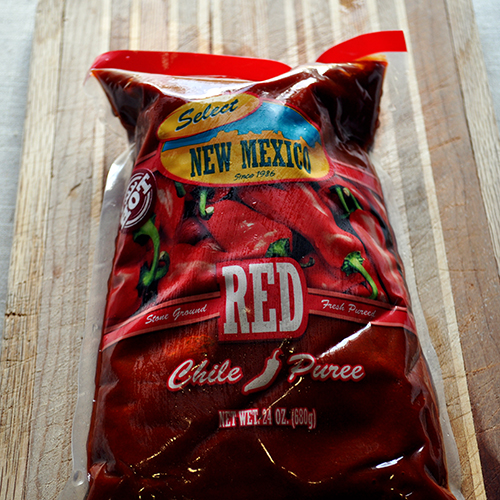 A bag of frozen red Chile paste on a wood cutting board. 