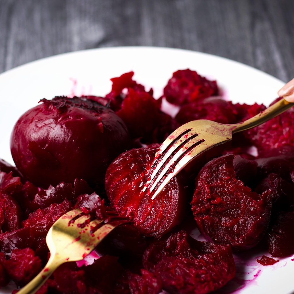 Someone using two forks to pull apart tender roasted beets.
