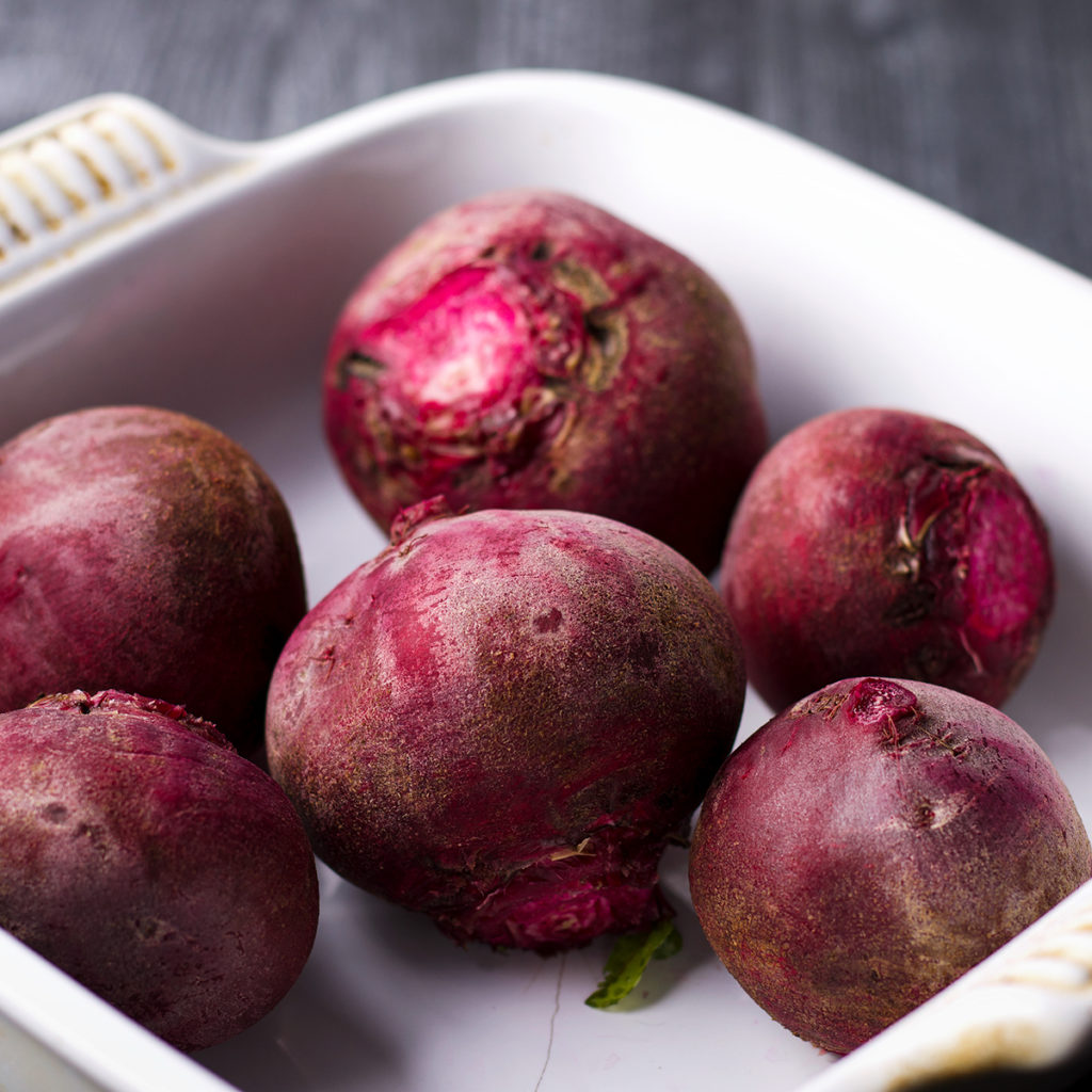 A white baking dish filled with fresh beets, ready to be roasted.