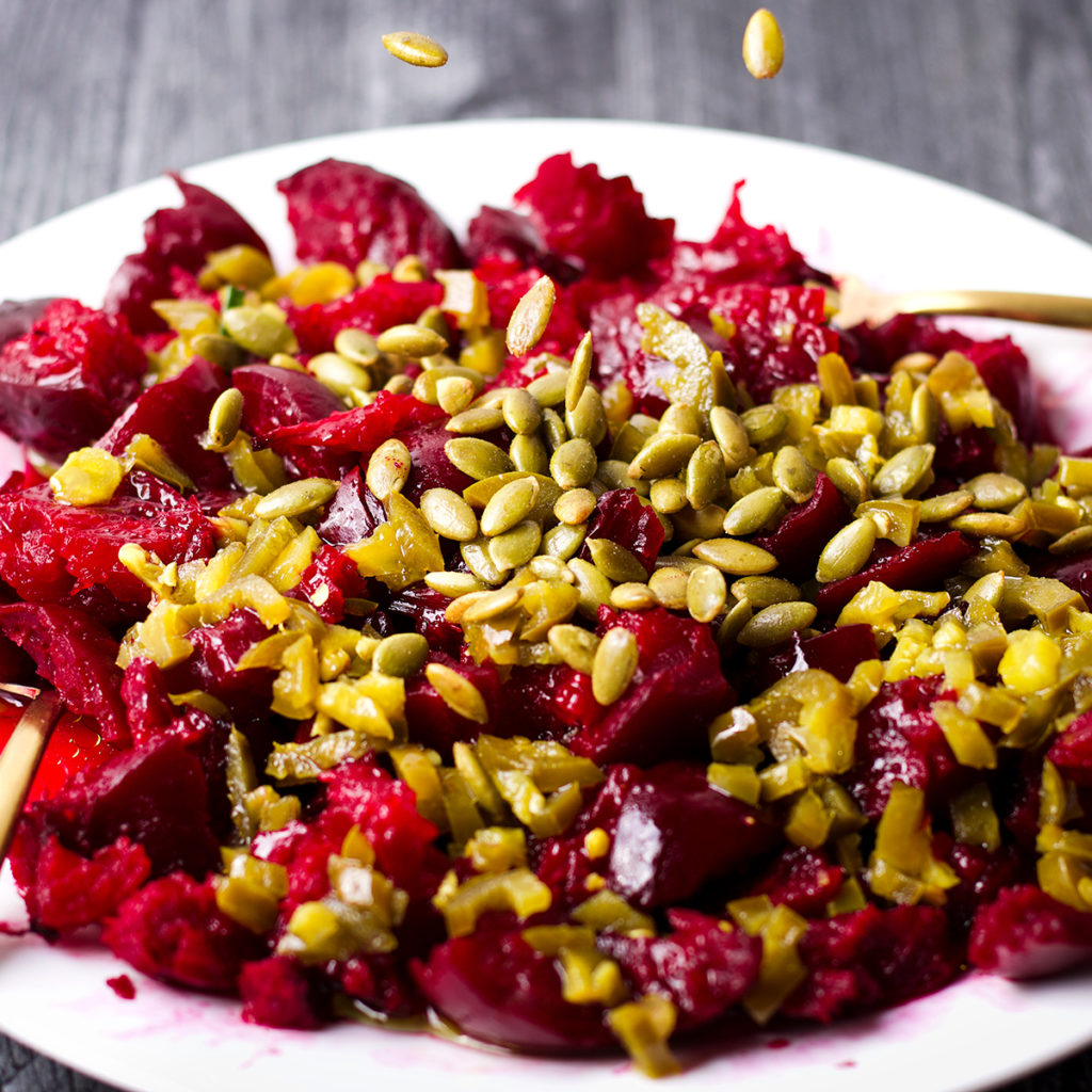 Sprinkling roasted pumpkin seeds over the top of a plate of roasted beets.