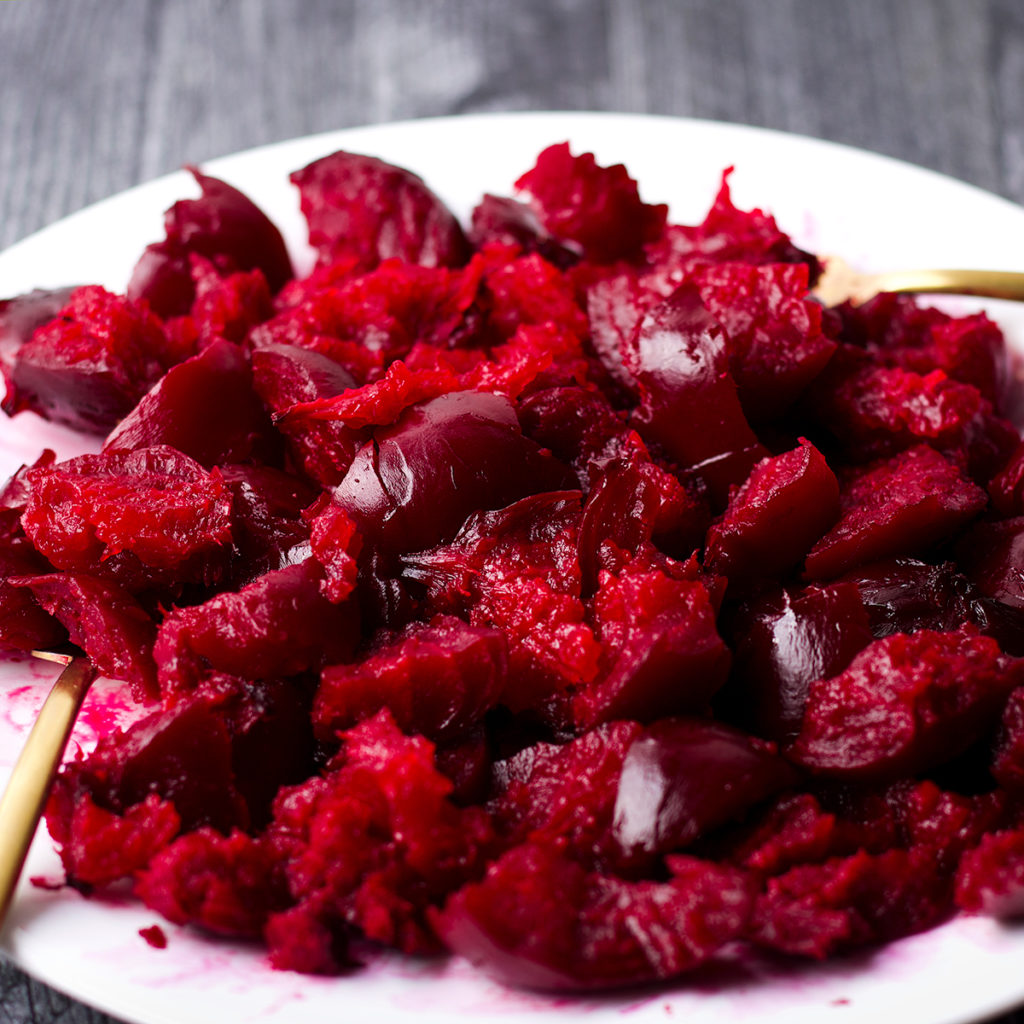 A plate of roasted beets that have been torn into bite size chunks for serving.