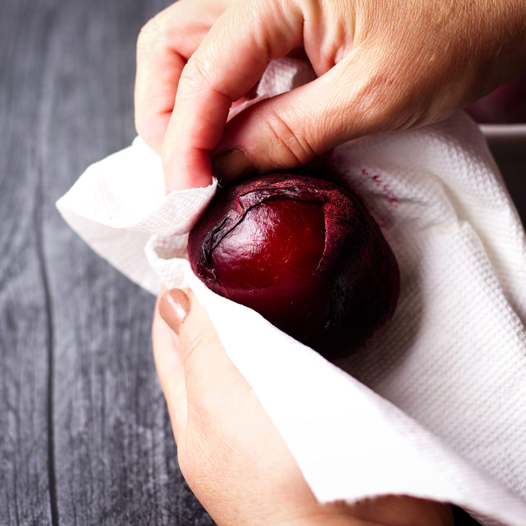 Someone using a paper towel to rub the skin from a roasted beet.