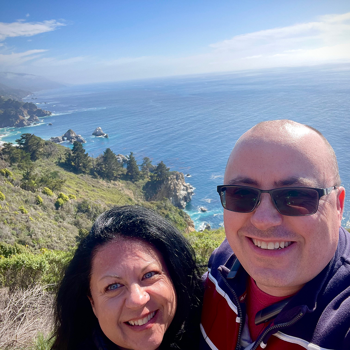 Steve and Rebecca Blackwell standing at the top of a cliffside overlooking the Pacific Ocean along the California coast.