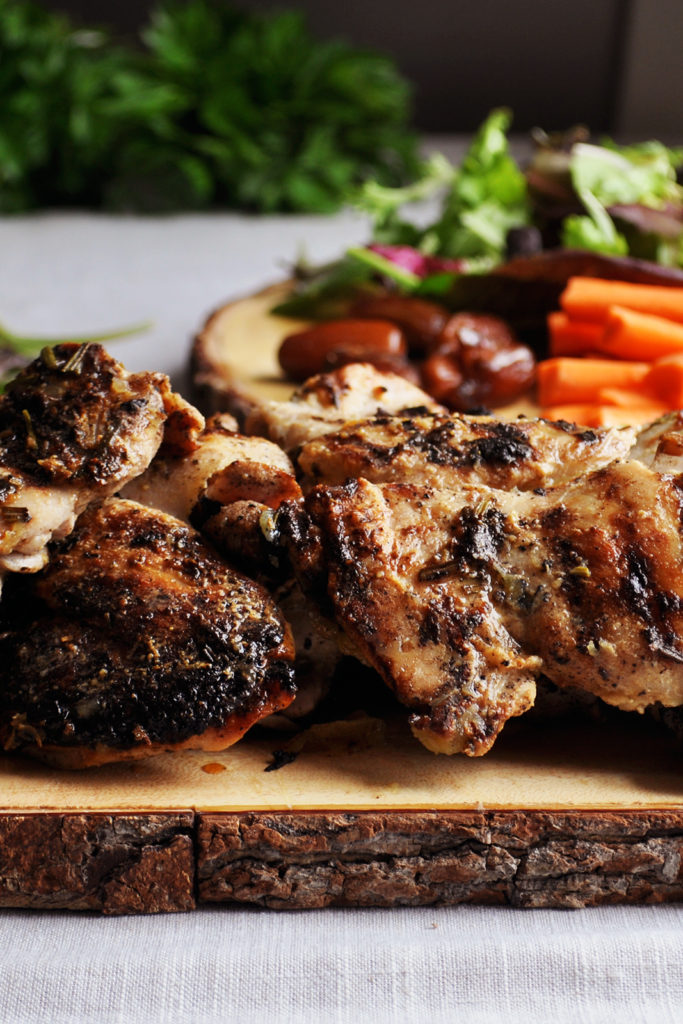 A wood tray piled with grilled lemon rosemary chicken. 
