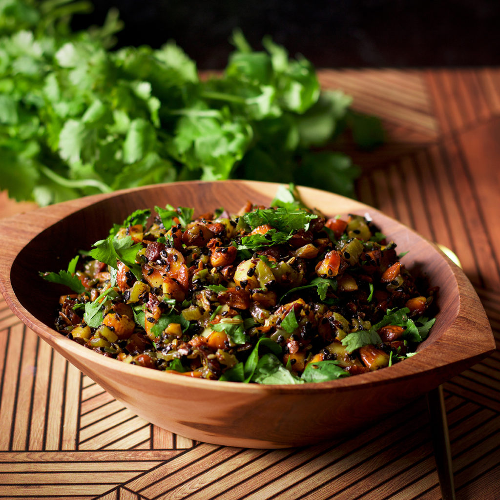 A wood bowl filled with almond salsa. The bowl is sitting on a wood table with a bunch of cilantro in the background.