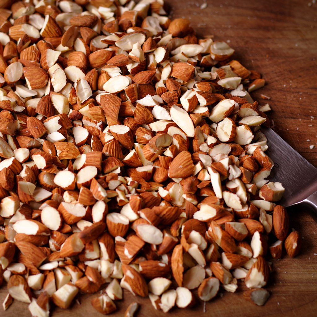 A pile of chopped almonds on a wood cutting board with a chef's knife.