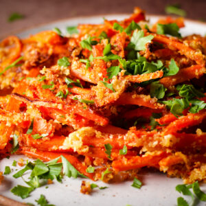 A plate of warm, crispy carrot fries topped with fresh parsley.