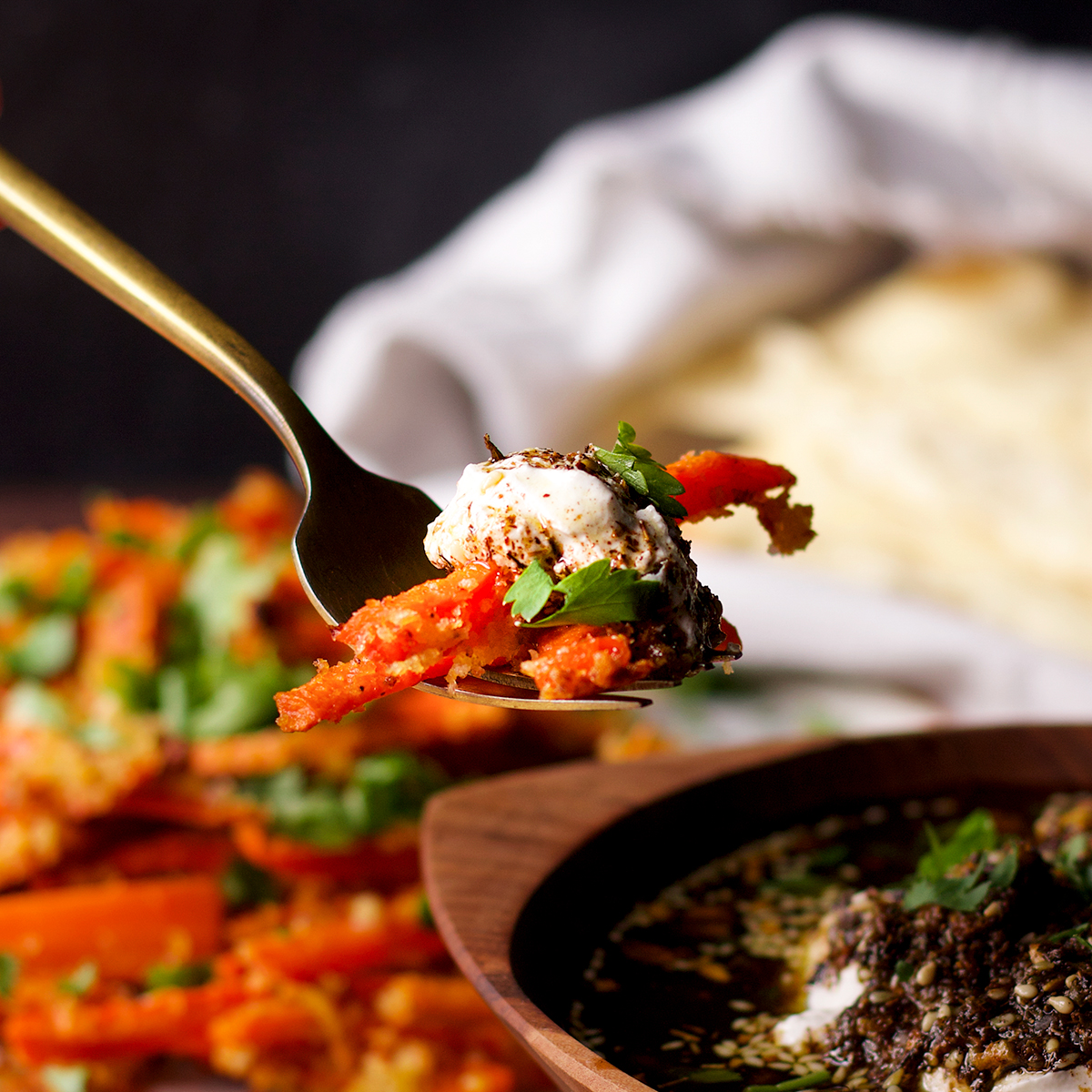 Someone lifting a forkful of carrot fries topped with a dollop of za'atar labneh.