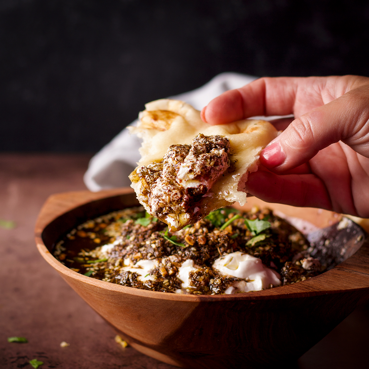 Someone dipping a piece of naan into a bowl filled with za'atar labneh.