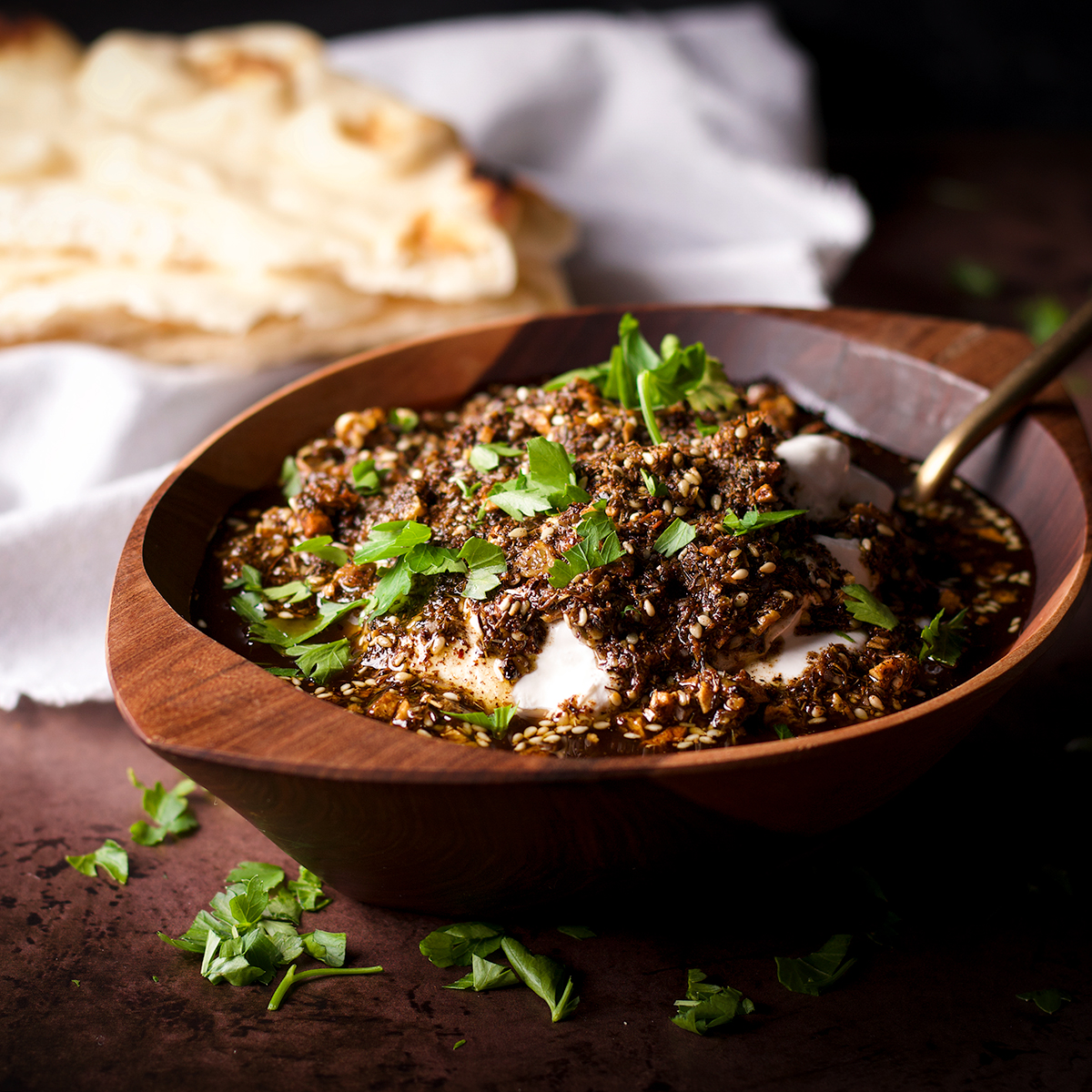 A wood bowl filled with za'atar labneh with crispy garlic sitting next to a stack of buttered naan.