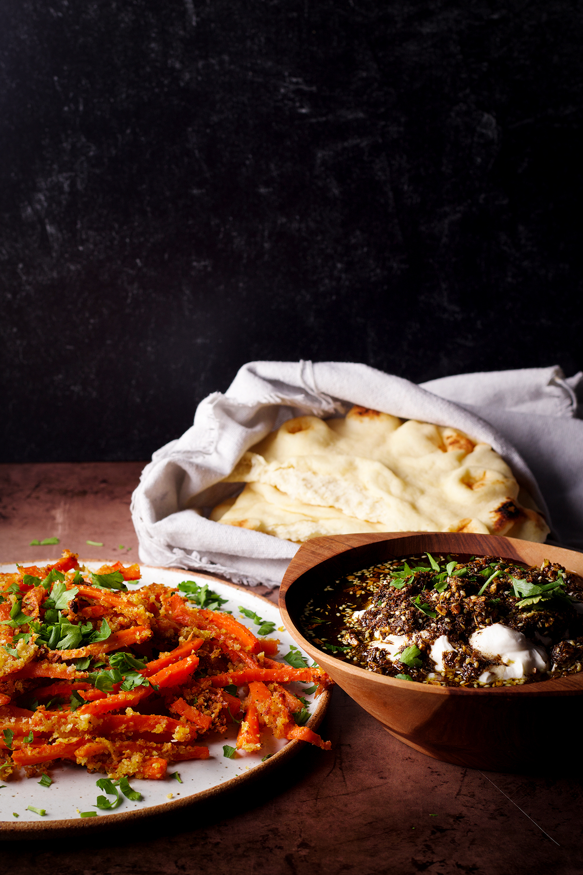 A bowl of za'atar labneh sitting next to a plate filled with carrot fries and a stack of buttered naan.