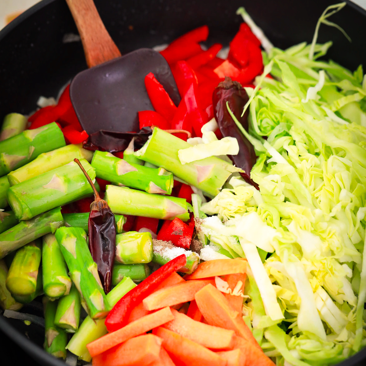 Someone using a spatula to stir vegetables in a skillet.