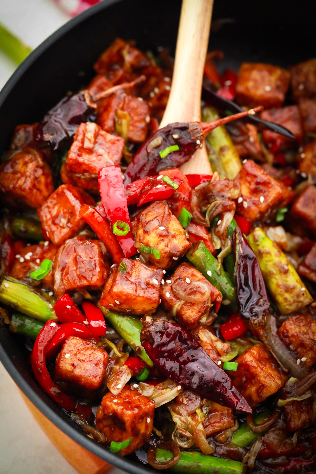 Someone using a wooden spoon to stir Szechuan Tofu and vegetables in a skillet.