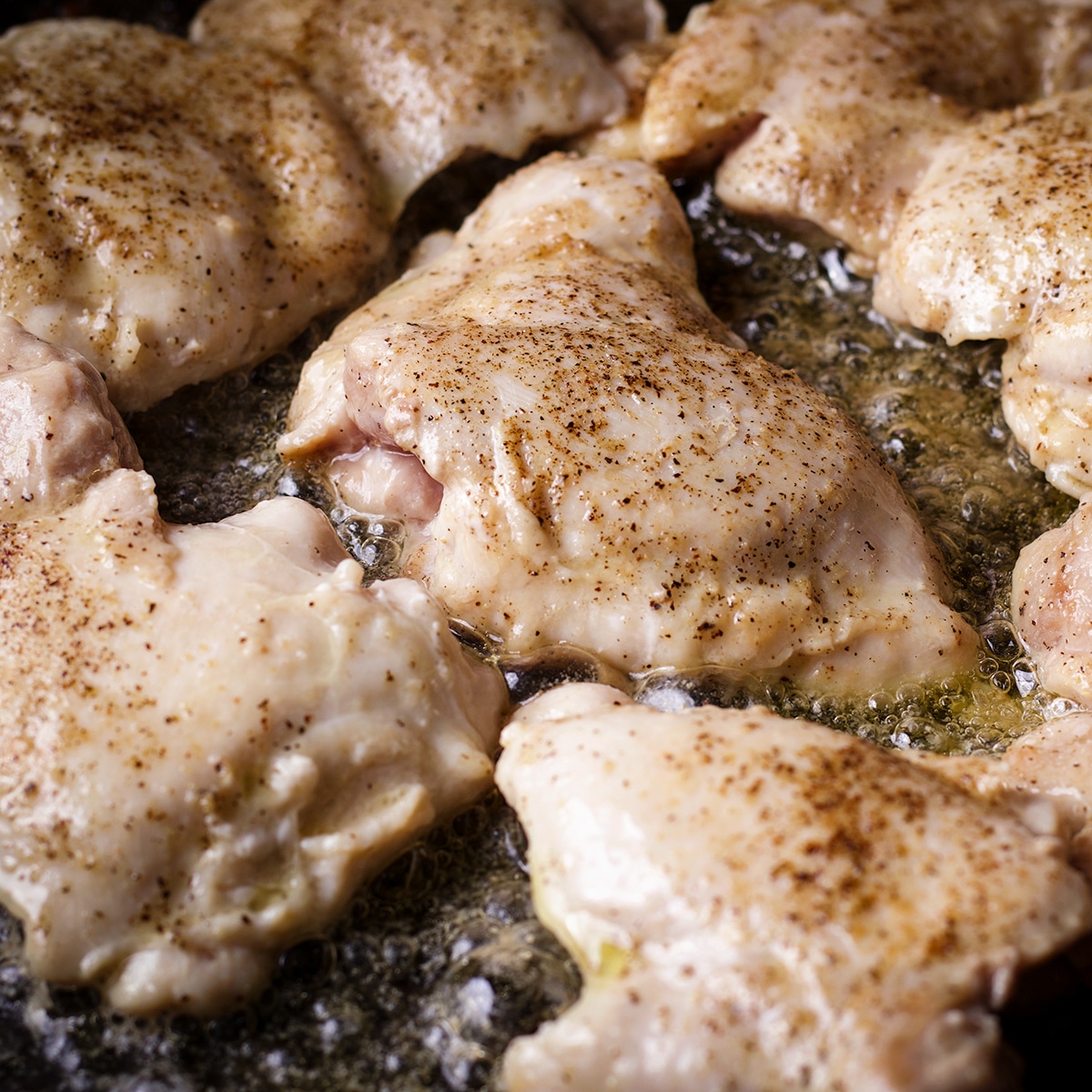 Boneless, skinless chicken thighs cooking in hot butter and oil until they are browned on the outside.