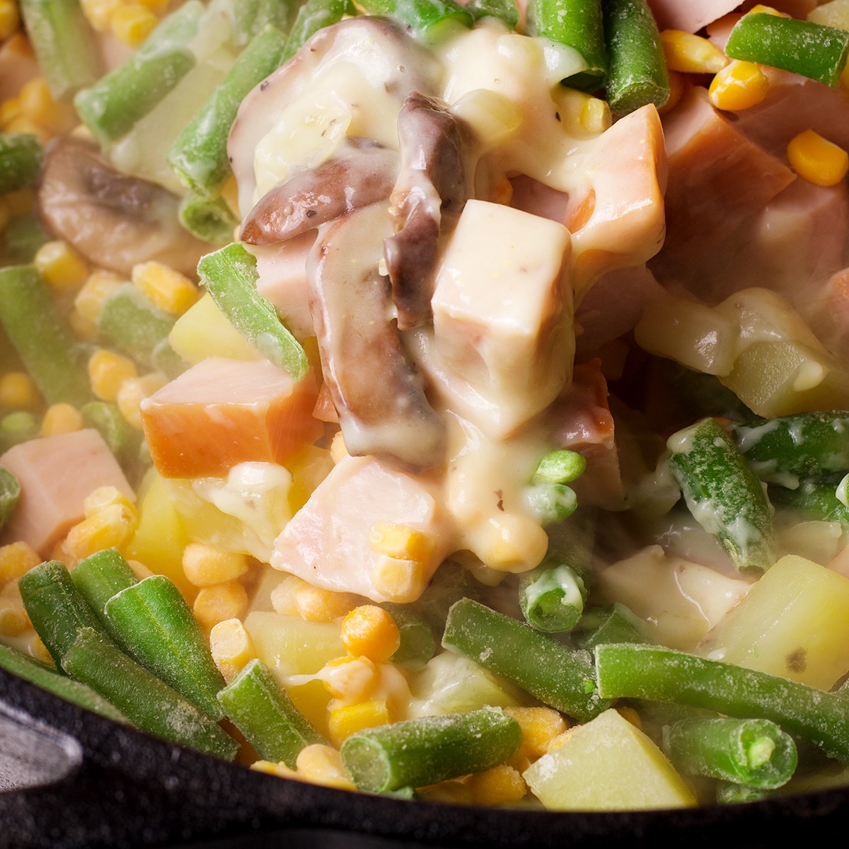 Looking down into a dutch oven while frozen vegetables are being added to pot pie filling.