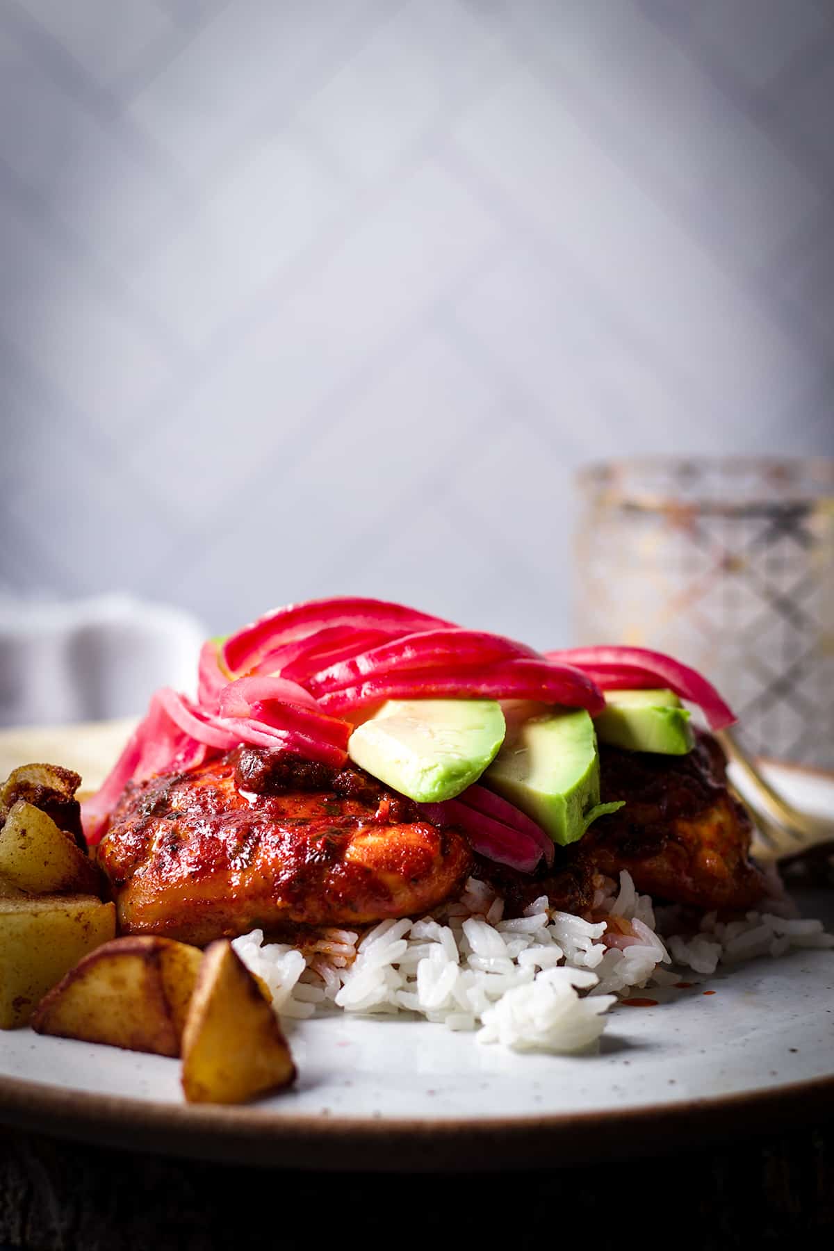 A close up photo of a plate of Mexican Adobo Chicken served over rice and topped with pickled red onions and fresh avocado.