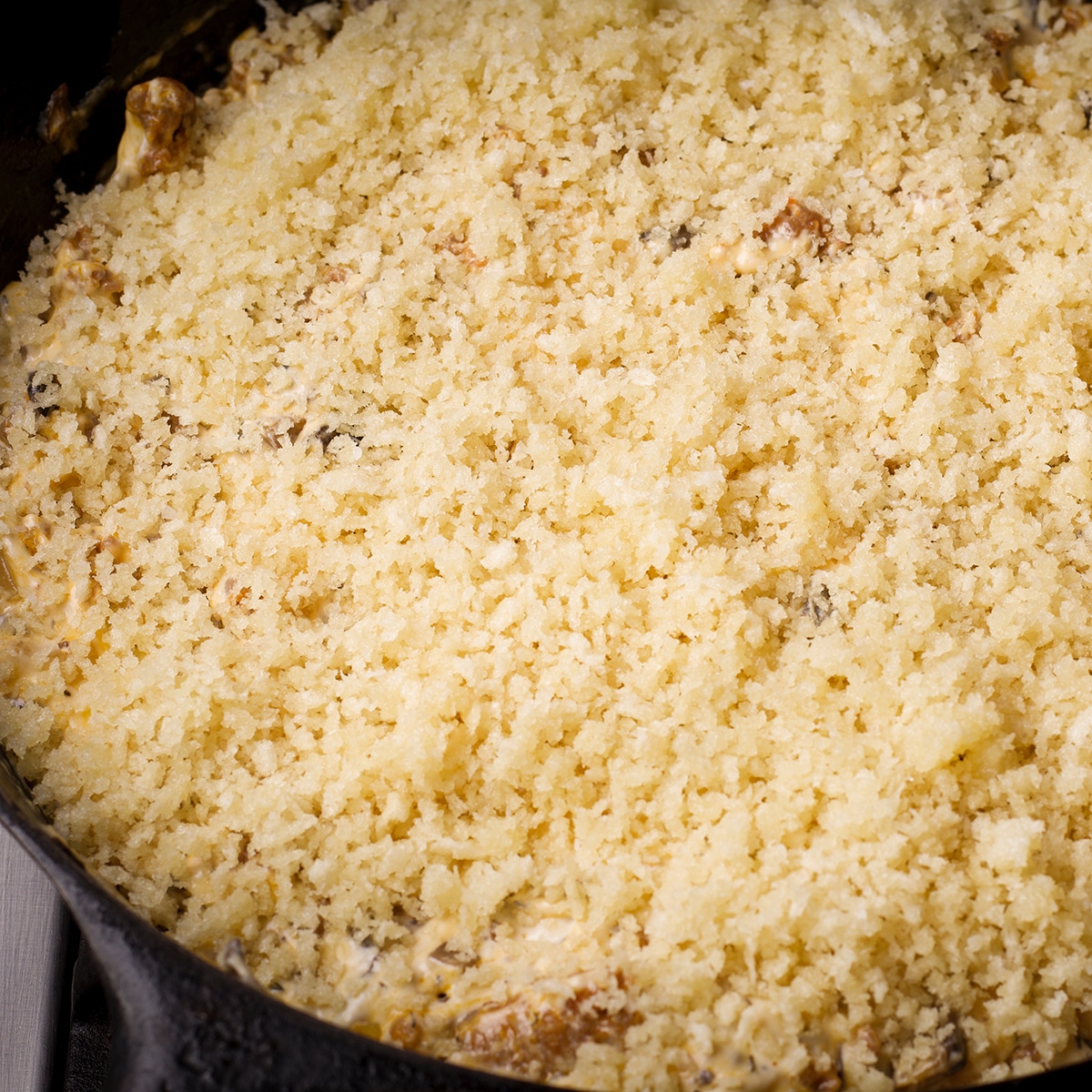 A cast iron skillet filled with stuffed mushroom dip and topped with panko bread crumbs.