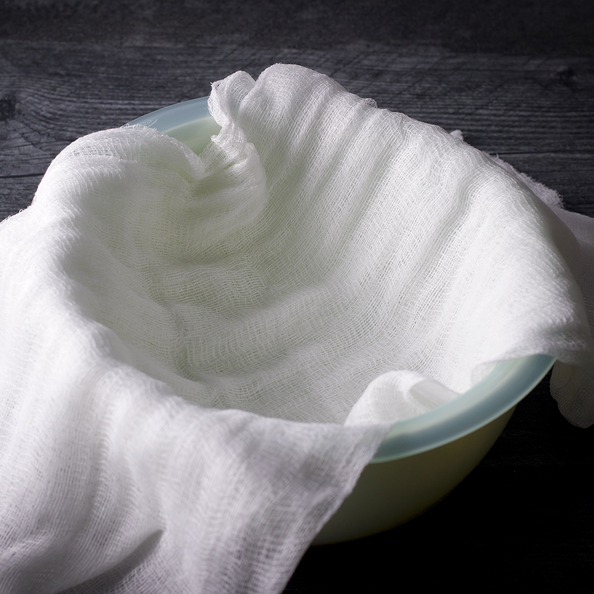 A cheesecloth lined strainer set inside a bowl.