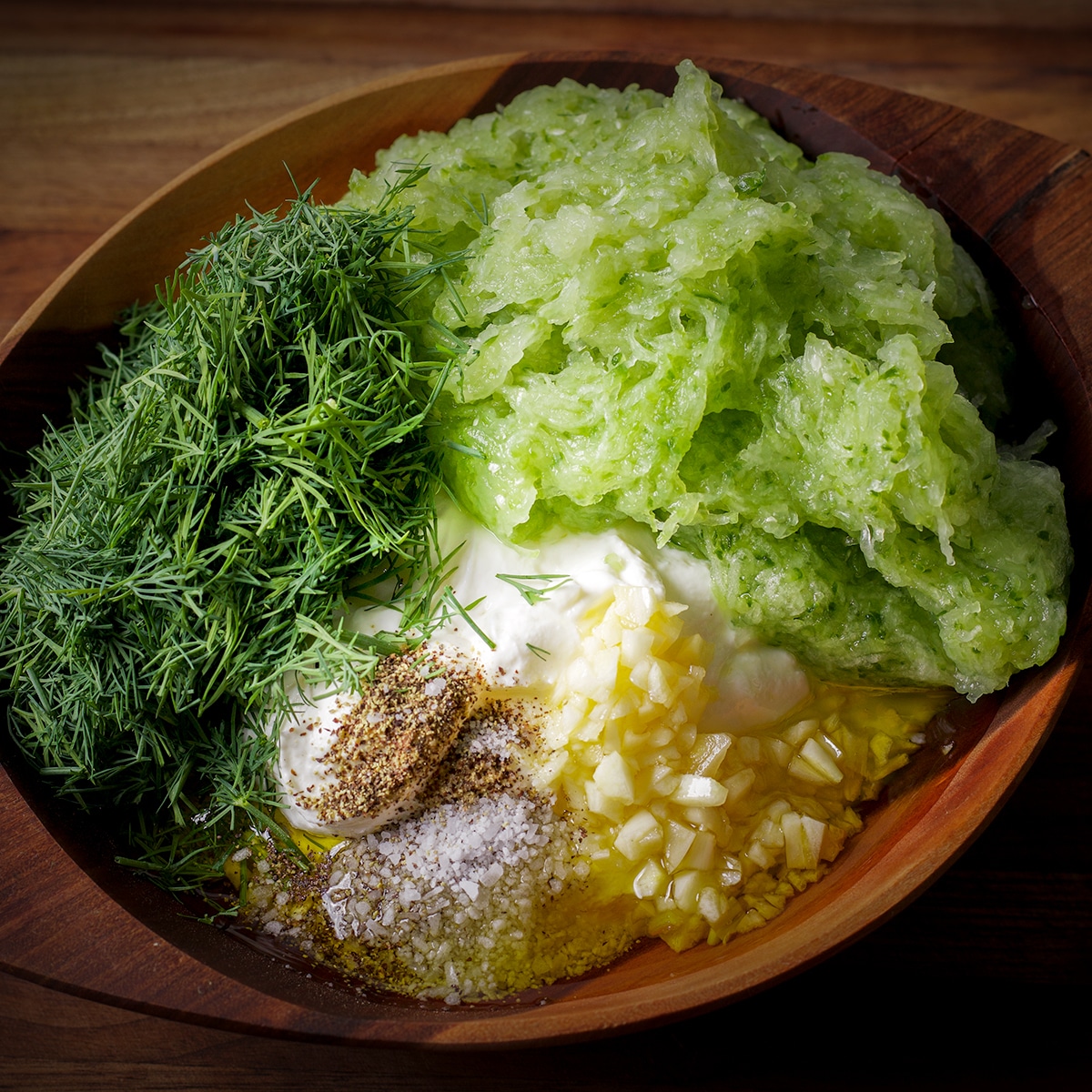 A wood bowl containing all the ingredients to make tzatziki sauce before the sauce is mixed.