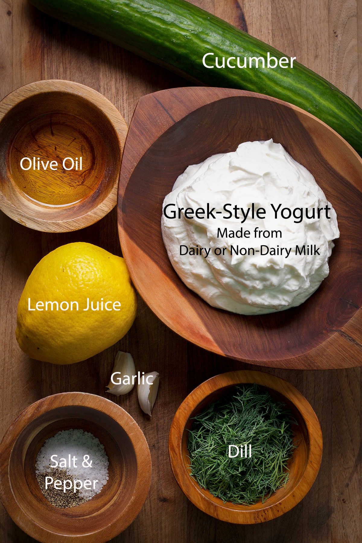 All of the ingredients to make traditional or vegan tzatziki on a wood cutting board.