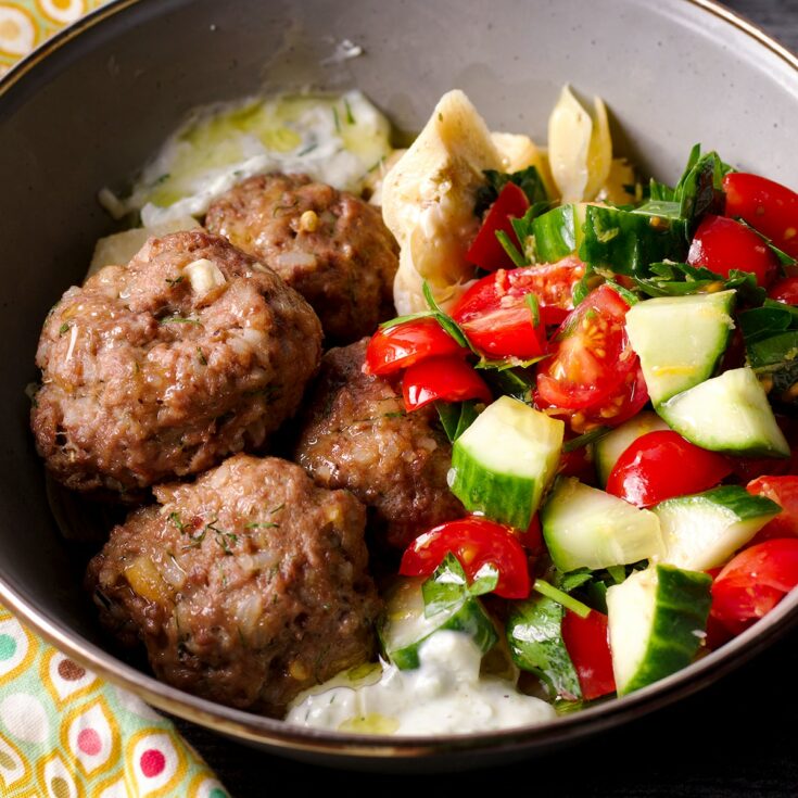 A bowl containing Greek meatballs and tzatziki sauce, and tomato and cucumber salad.