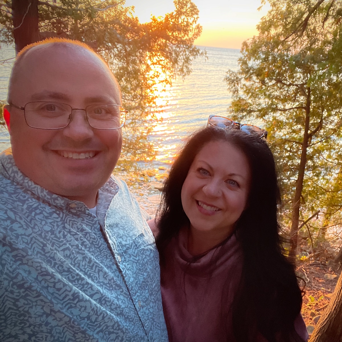 Steve and Rebecca Blackwell standing on the coast of Door County with the sun setting over the water behind them.