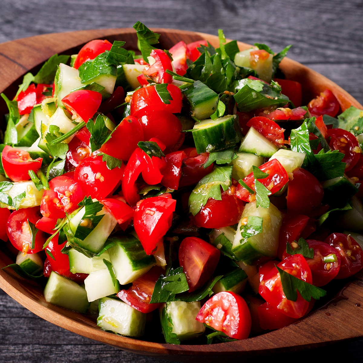 A wood bowl containing tomato and cucumber salad.