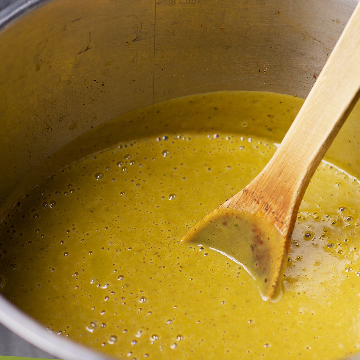 Someone using a wooden spoon to stir a pot of creamy broccoli soup as it simmers in a stock pot.
