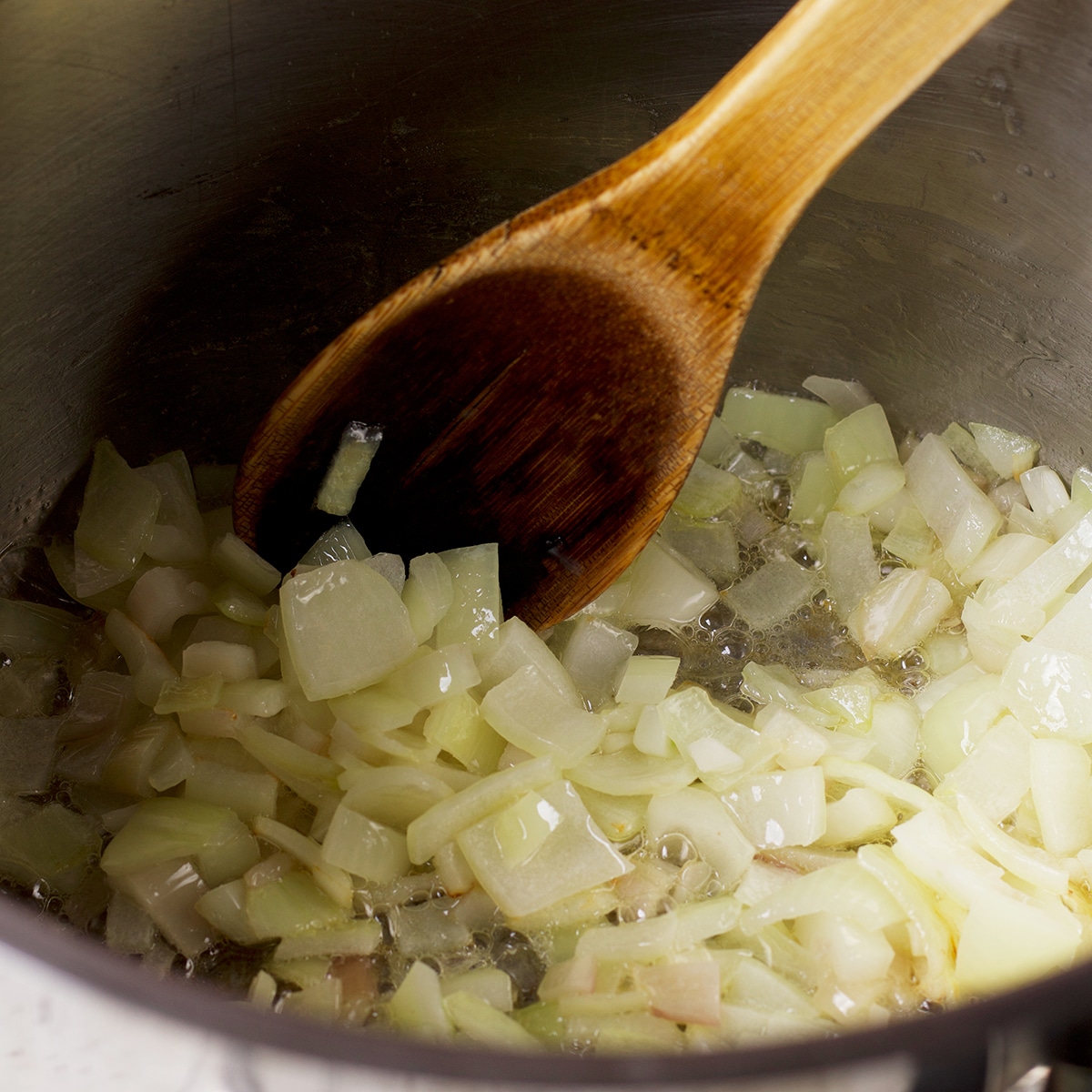 Someone using a wooden spoon to stir onions as they cook in a stock pot.