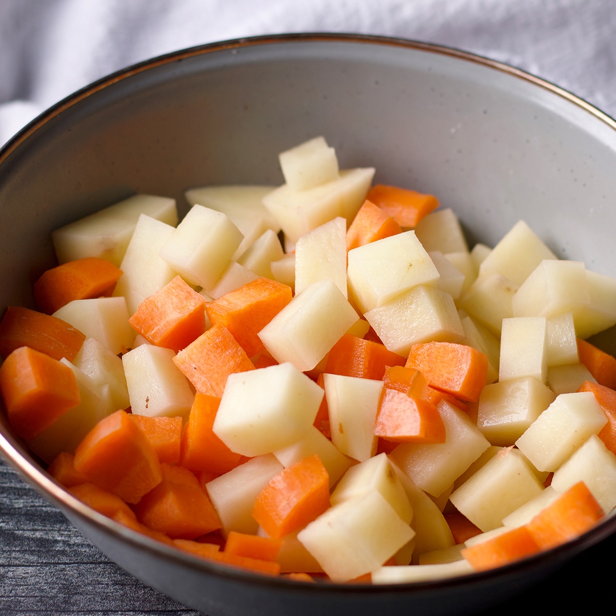 A blue bowl filled with chopped potatoes and carrots.