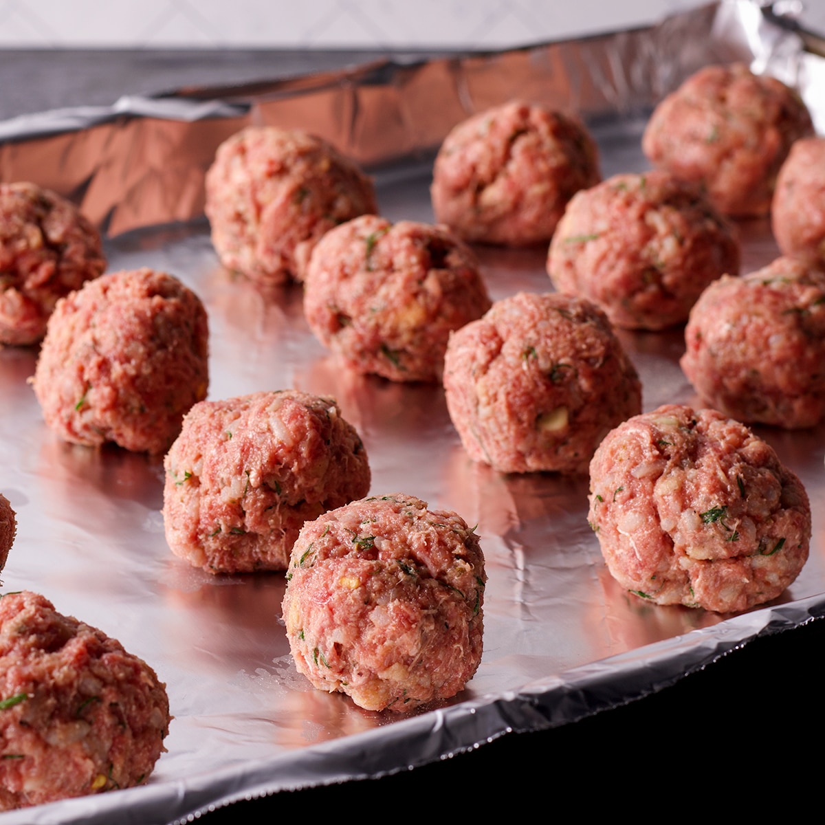 Raw Greek meatballs on a foil lined baking sheet ready to go in the oven.