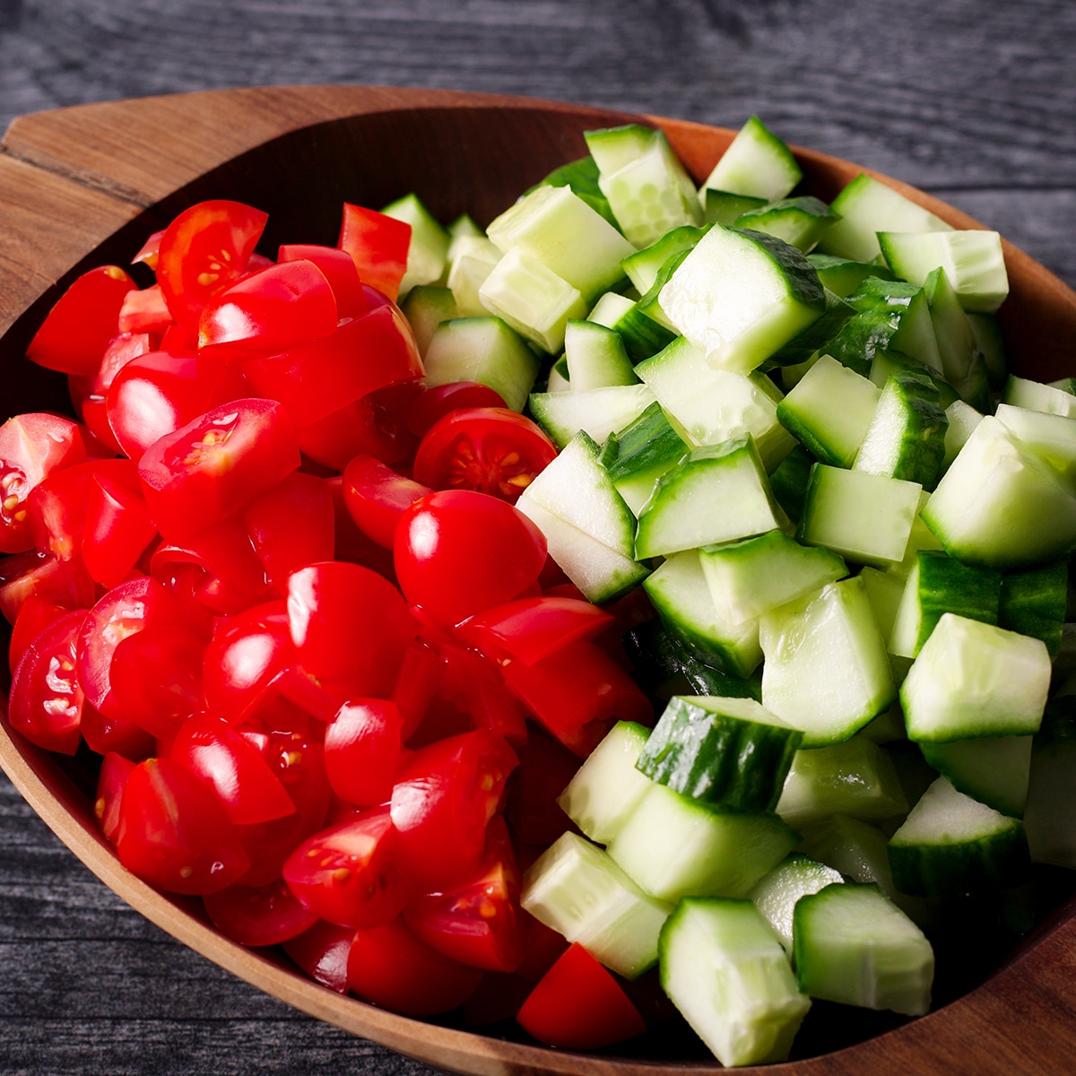 Chopped cherry tomatoes and cucumbers in a wood bowl.