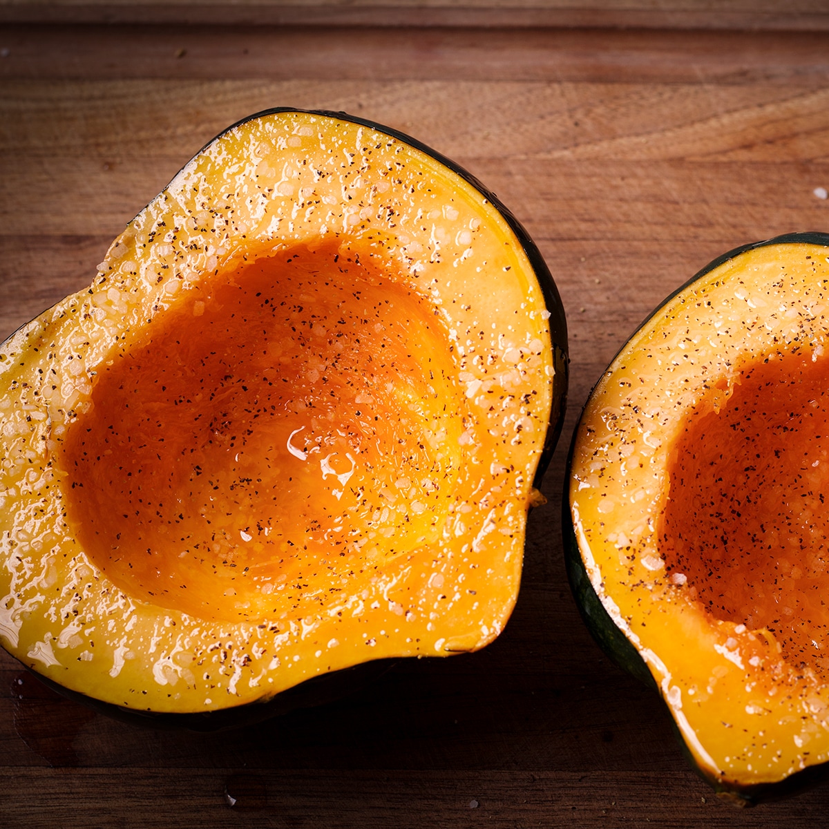 An acorn squash that's been cut in half and brushed with olive oil and sprinkled with salt and pepper.