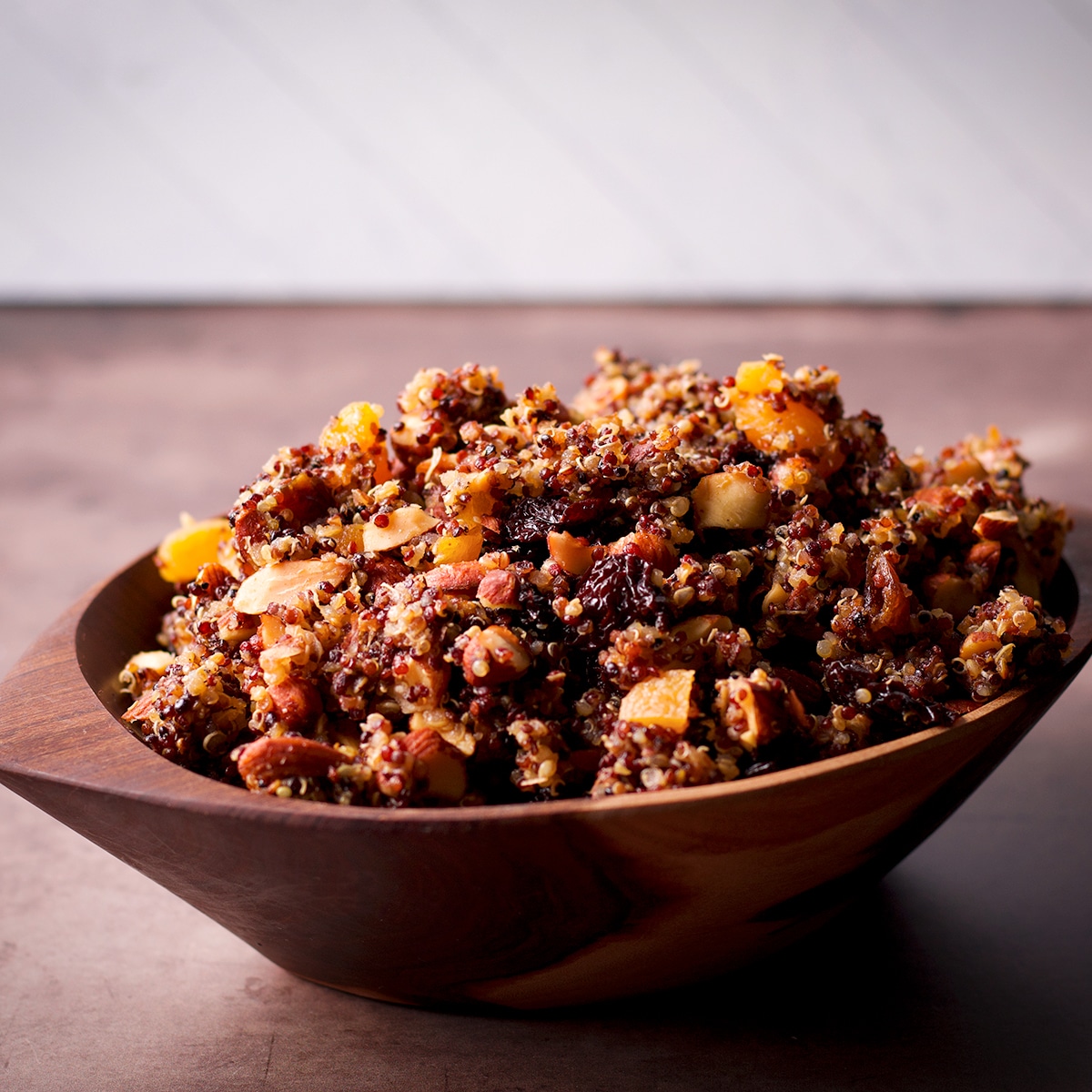 A wood bowl filled with cooked quinoa mixed with chopped nuts and dried fruit.