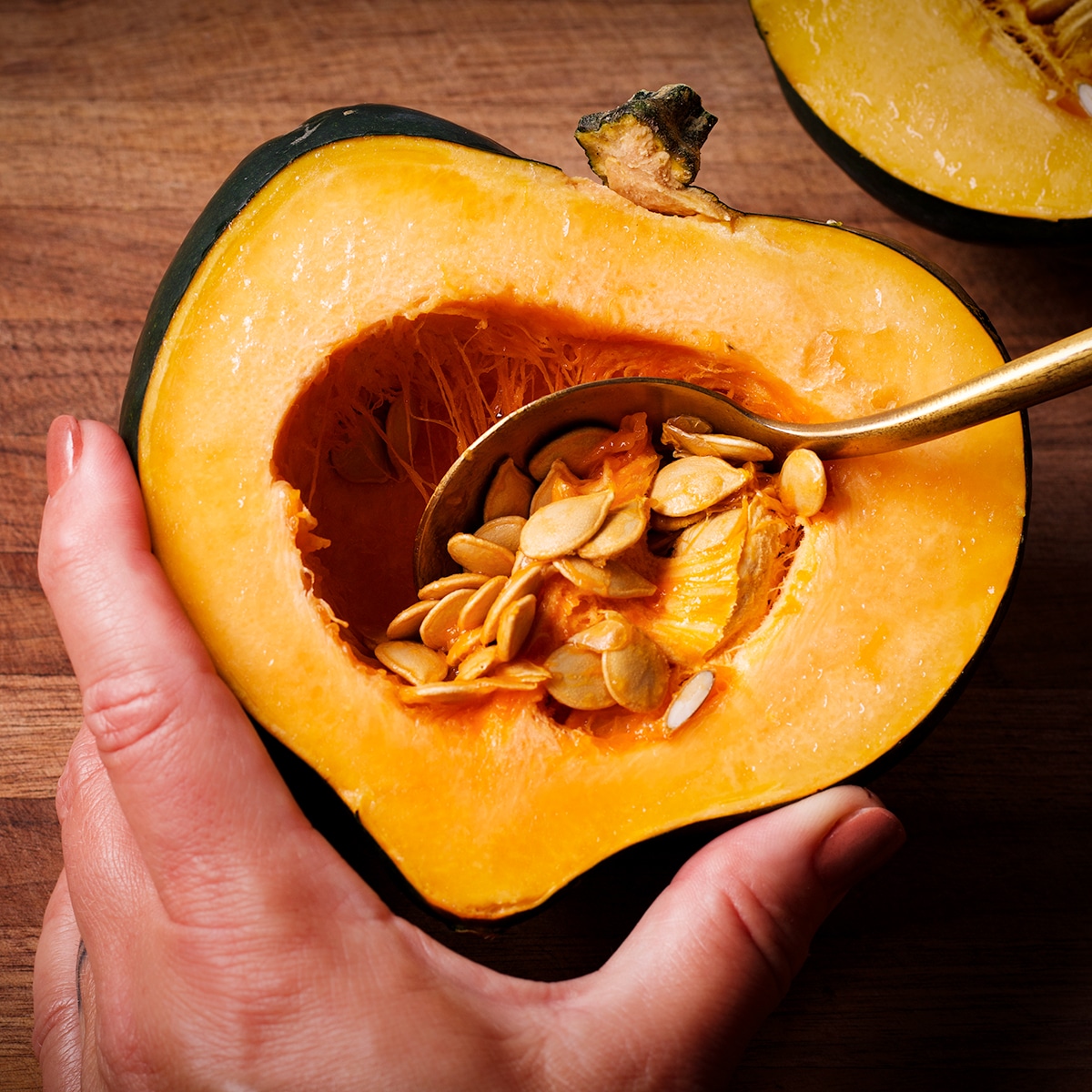Someone using a spoon to scoop the seeds out of the center of an acorn squash.