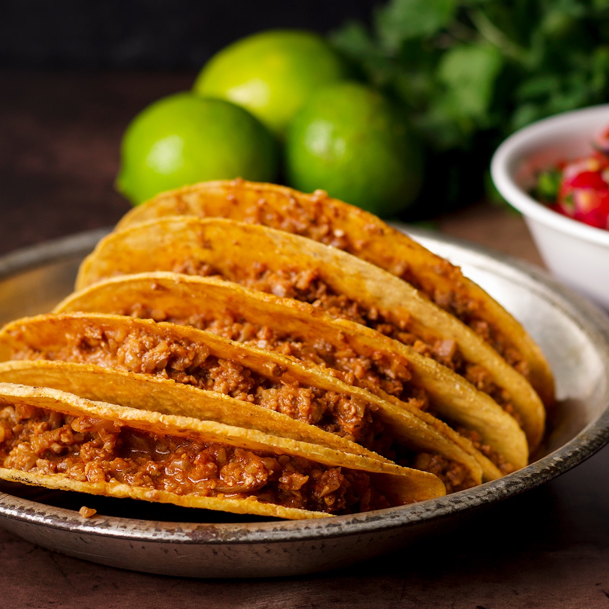 A tin plate filled with hard shell tacos stuffed with vegan taco meat.