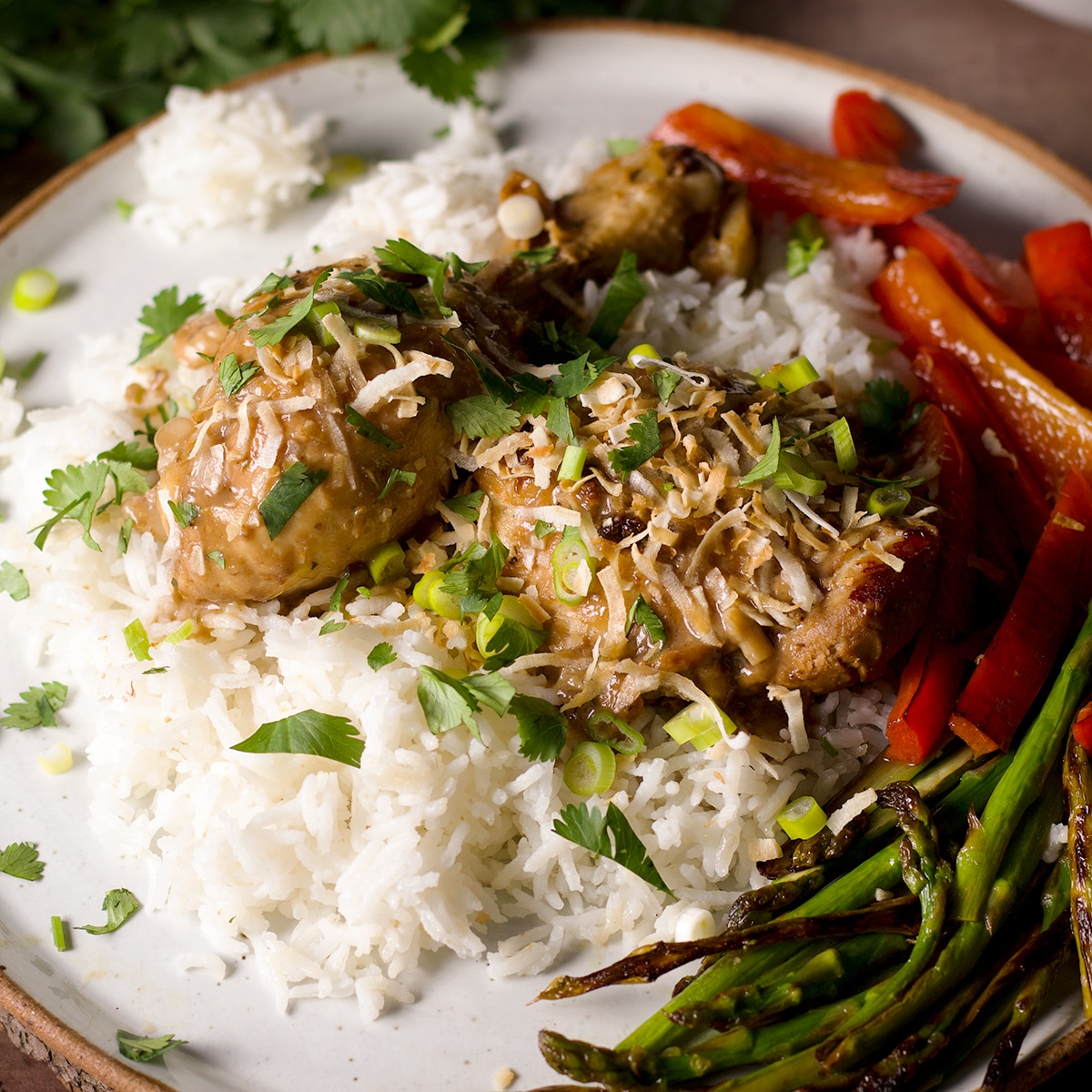 A plate containing Filipino chicken adobo with coconut milk served with sautéed vegetables over rice.