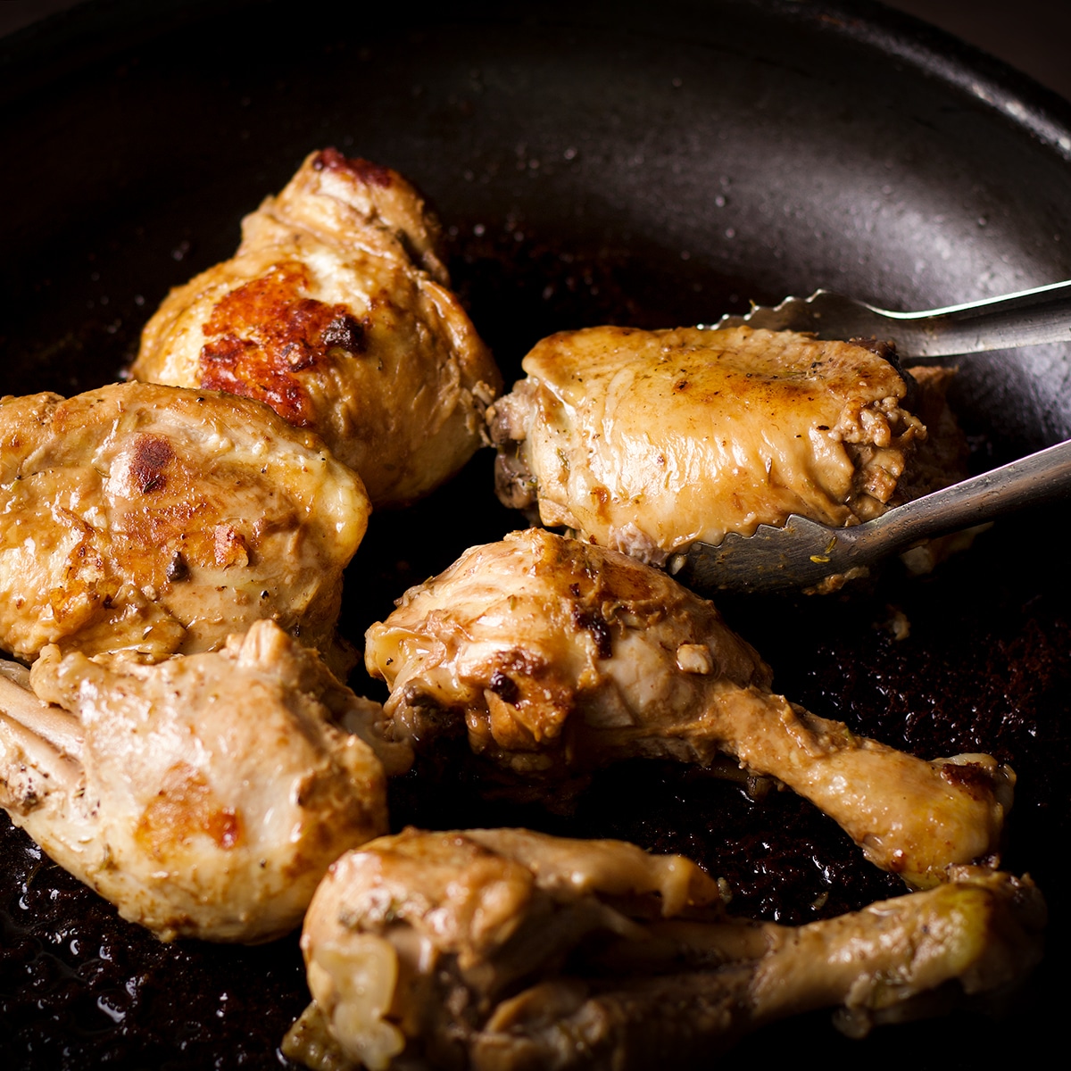 Searing pieces of chicken in a hot skillet after marinating it in filipino style coconut adobo sauce.