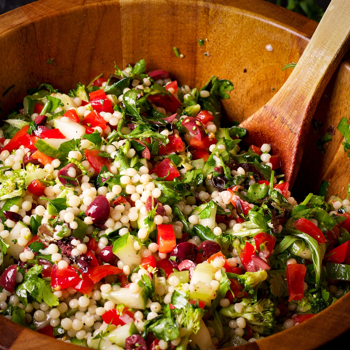 Using a wooden spoon to toss all the ingredients together for Vegan Pearl Couscous Salad.