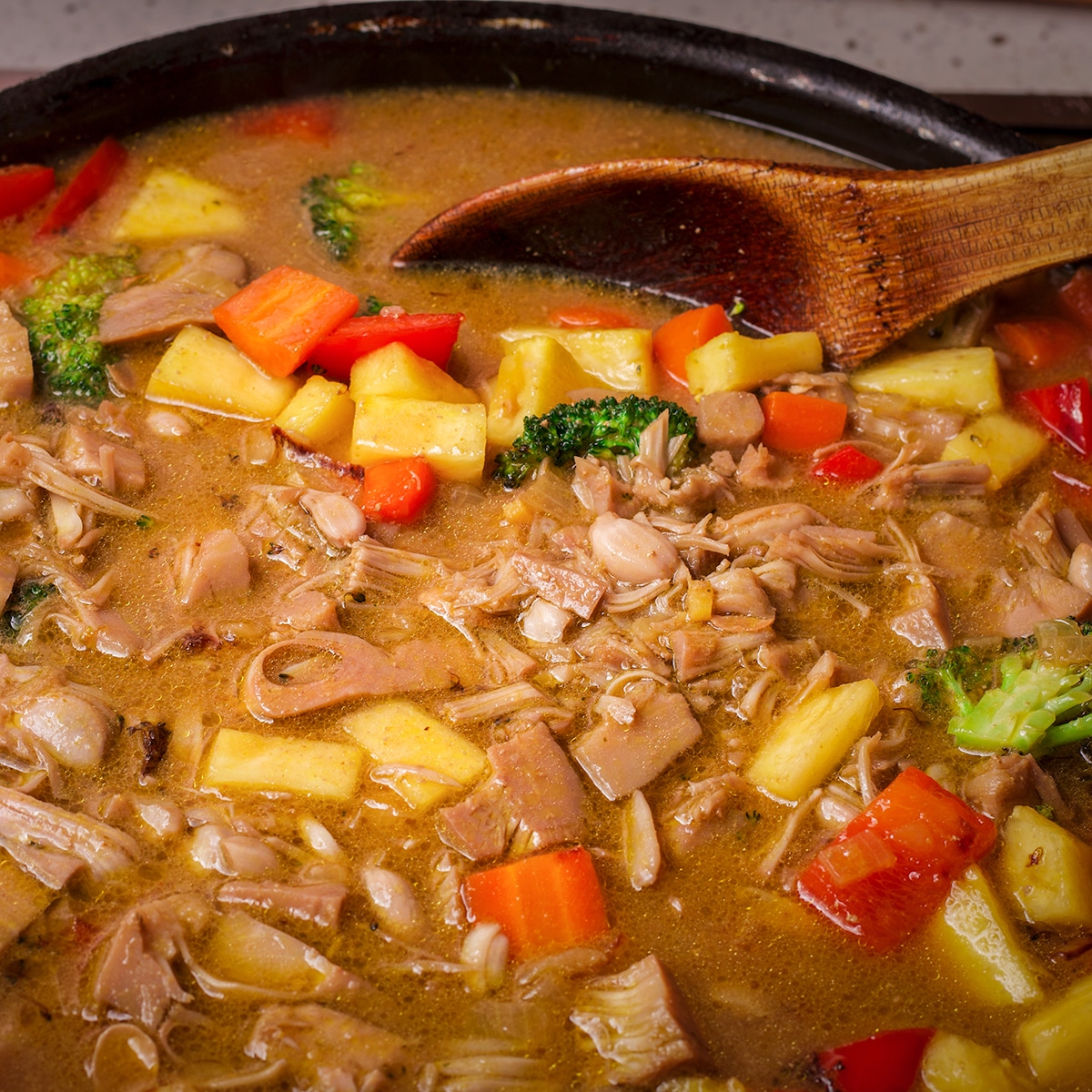 Using a wooden spoon to stir jackfruit curry in a large skillet.