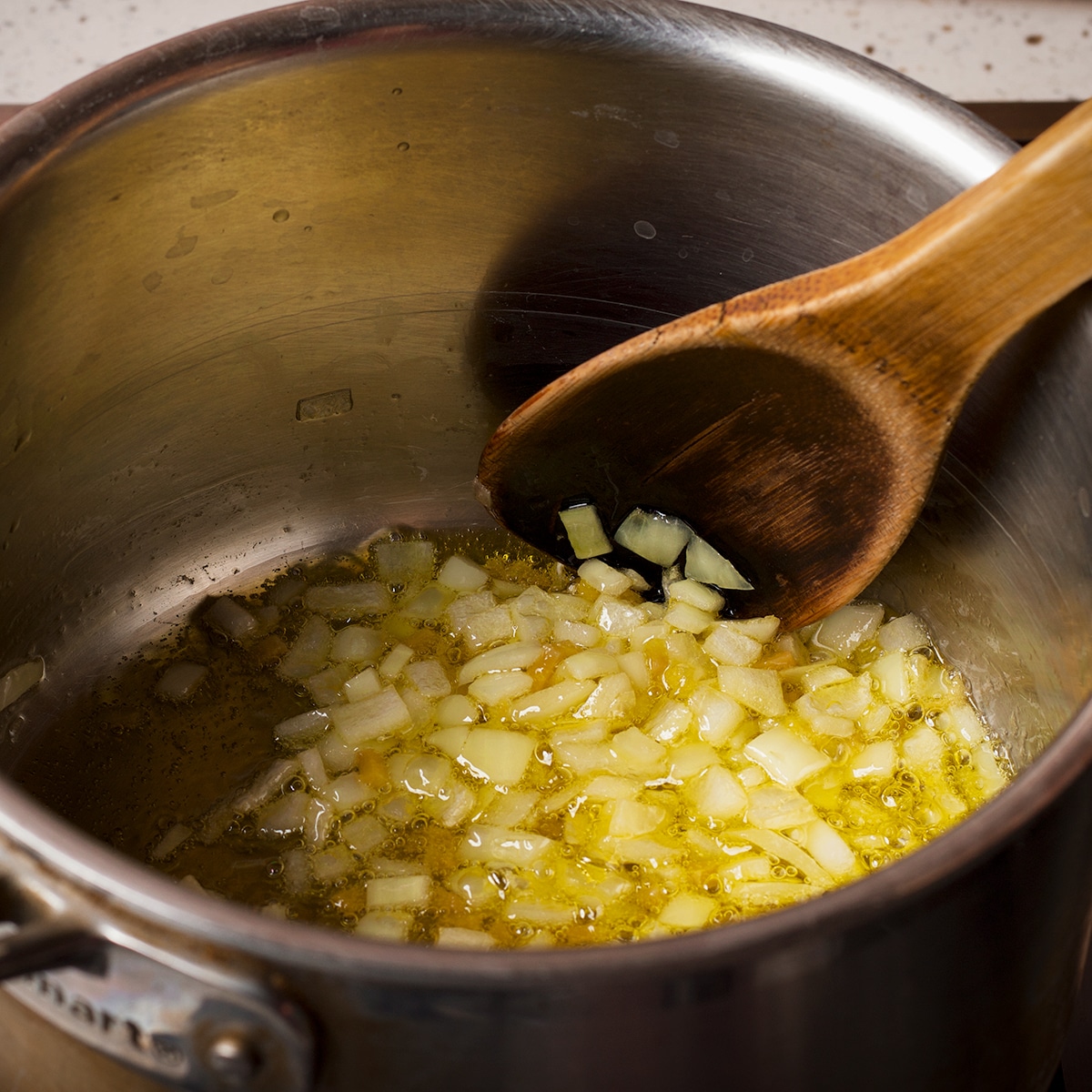 Using a wooden spoon to stir chopped onions and shallots in a saucepan.