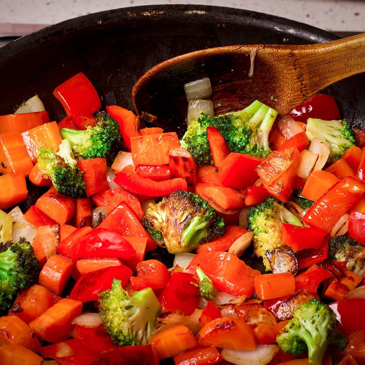 Using a wooden spoon to stir vegetables as they cook in a skillet. 