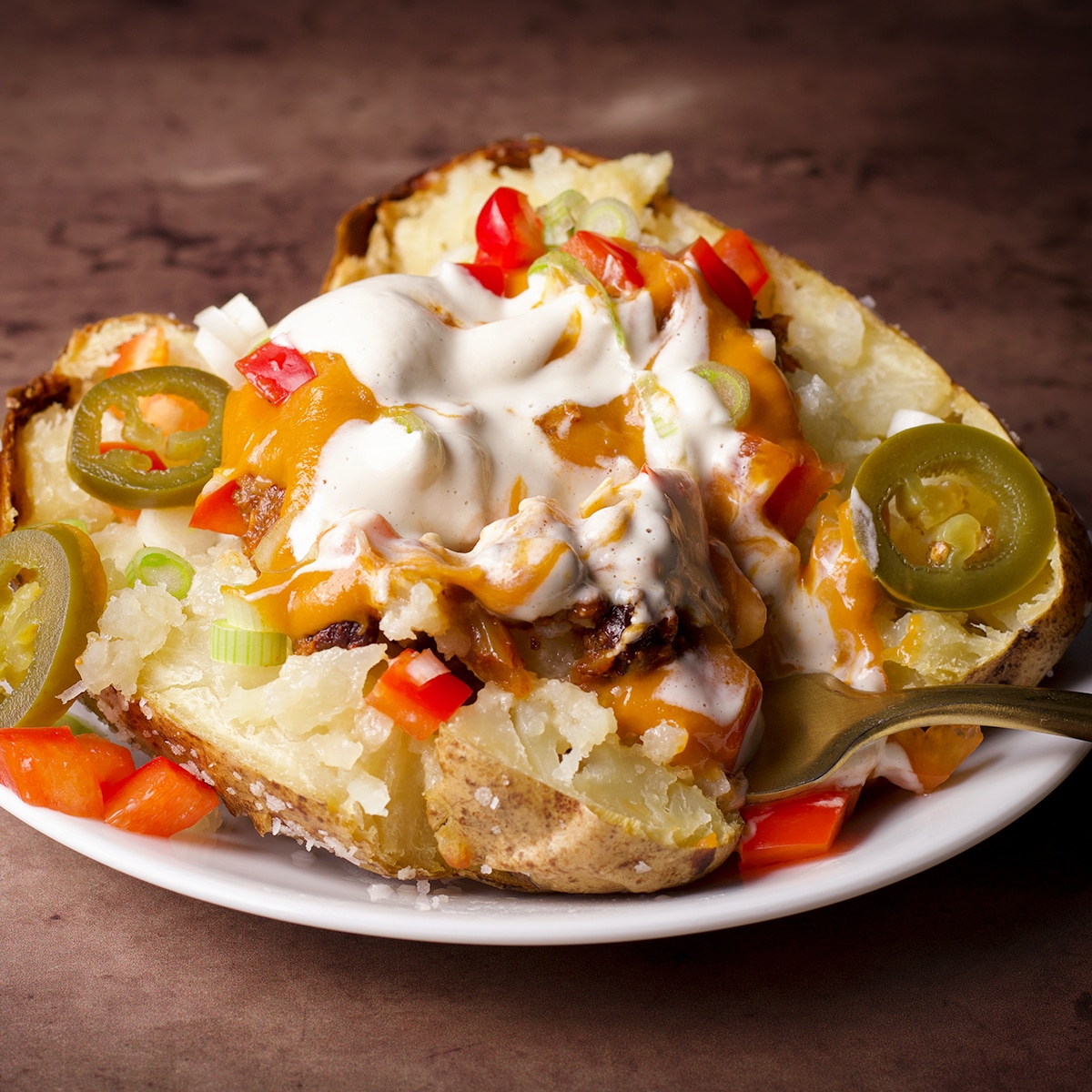 A baked potato loaded with vegan taco meat, vegan nacho cheese sauce, vegan sour cream, and chopped veggies.