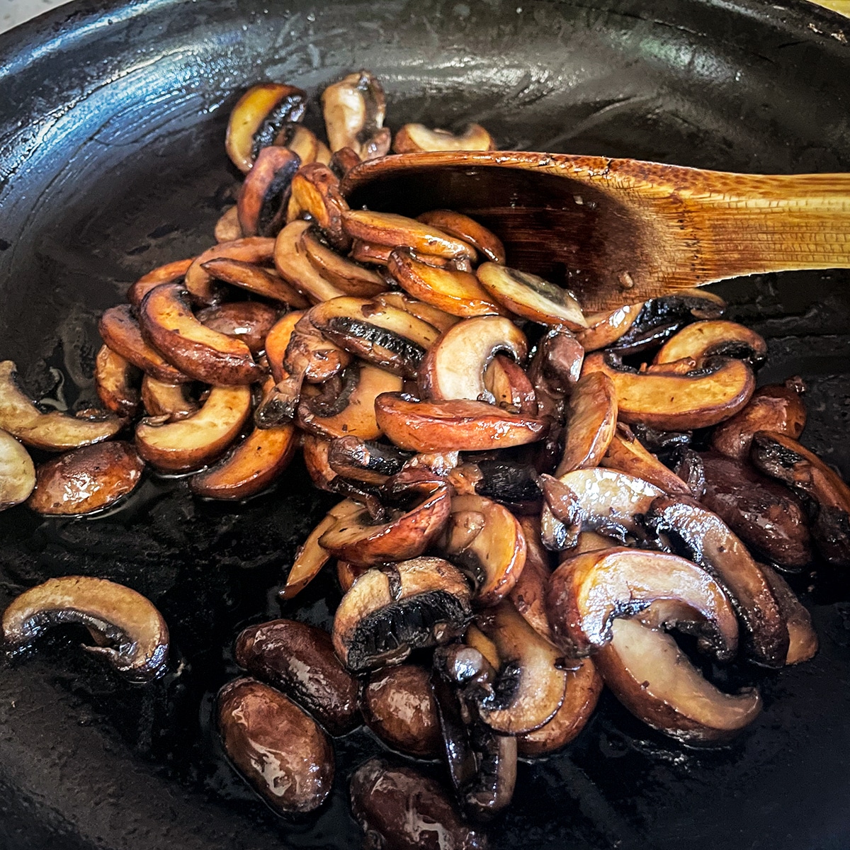 Sliced mushrooms cooking in a hot skillet until they are caramelized.