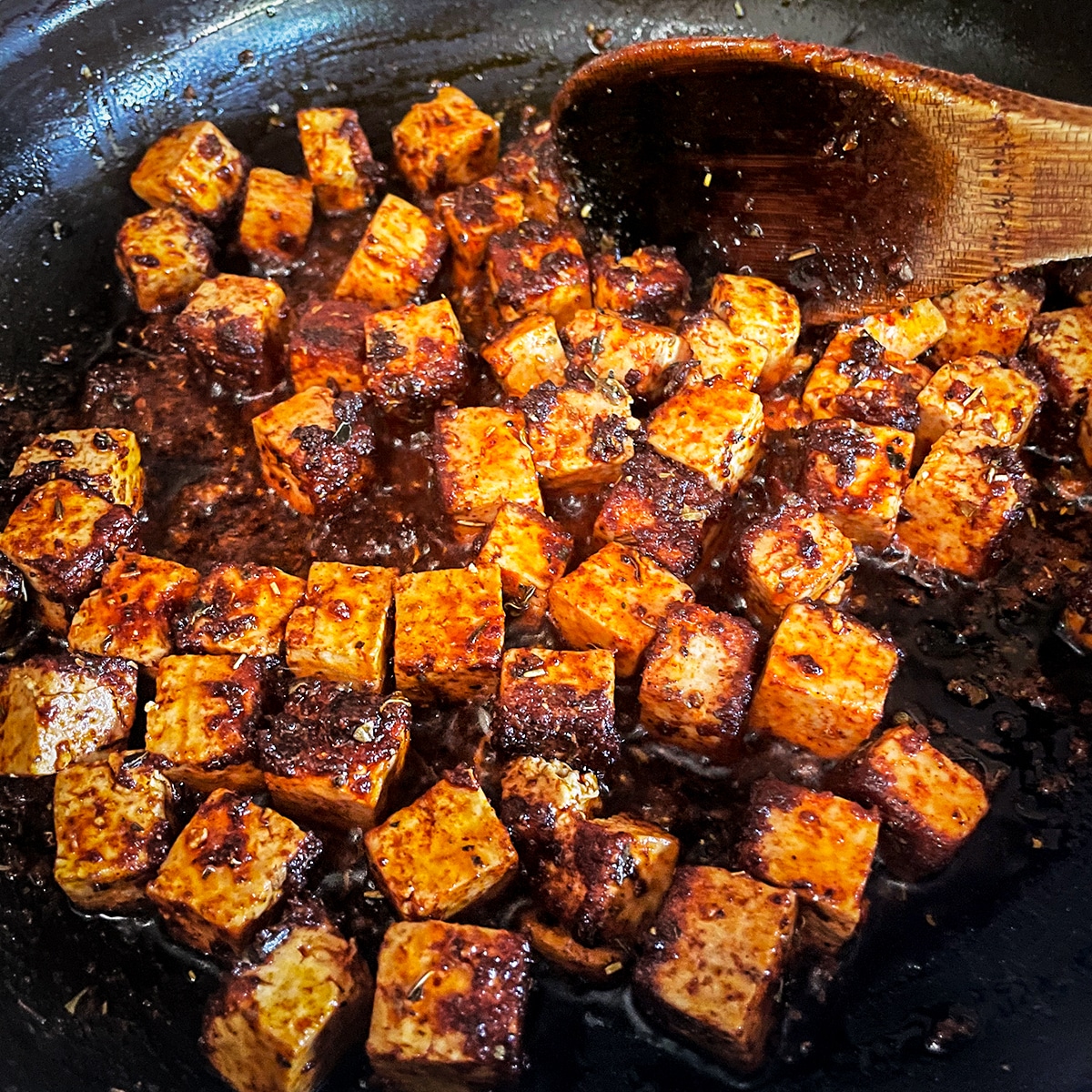 Pieces of spice covered tofu cooking in a skillet until they are crispy.