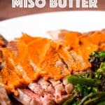 A white plate containing sliced flank steak smothered in miso butter and grilled vegetables.