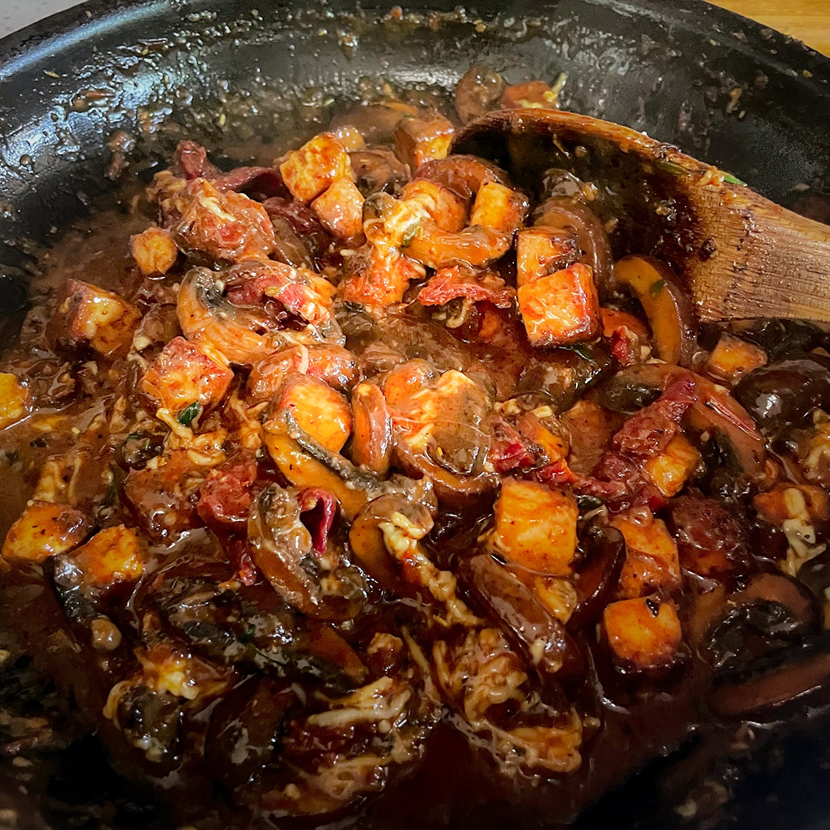 Stirring cooked crispy tofu into the skillet with mushrooms coated in creamy sun-dried tomato sauce.