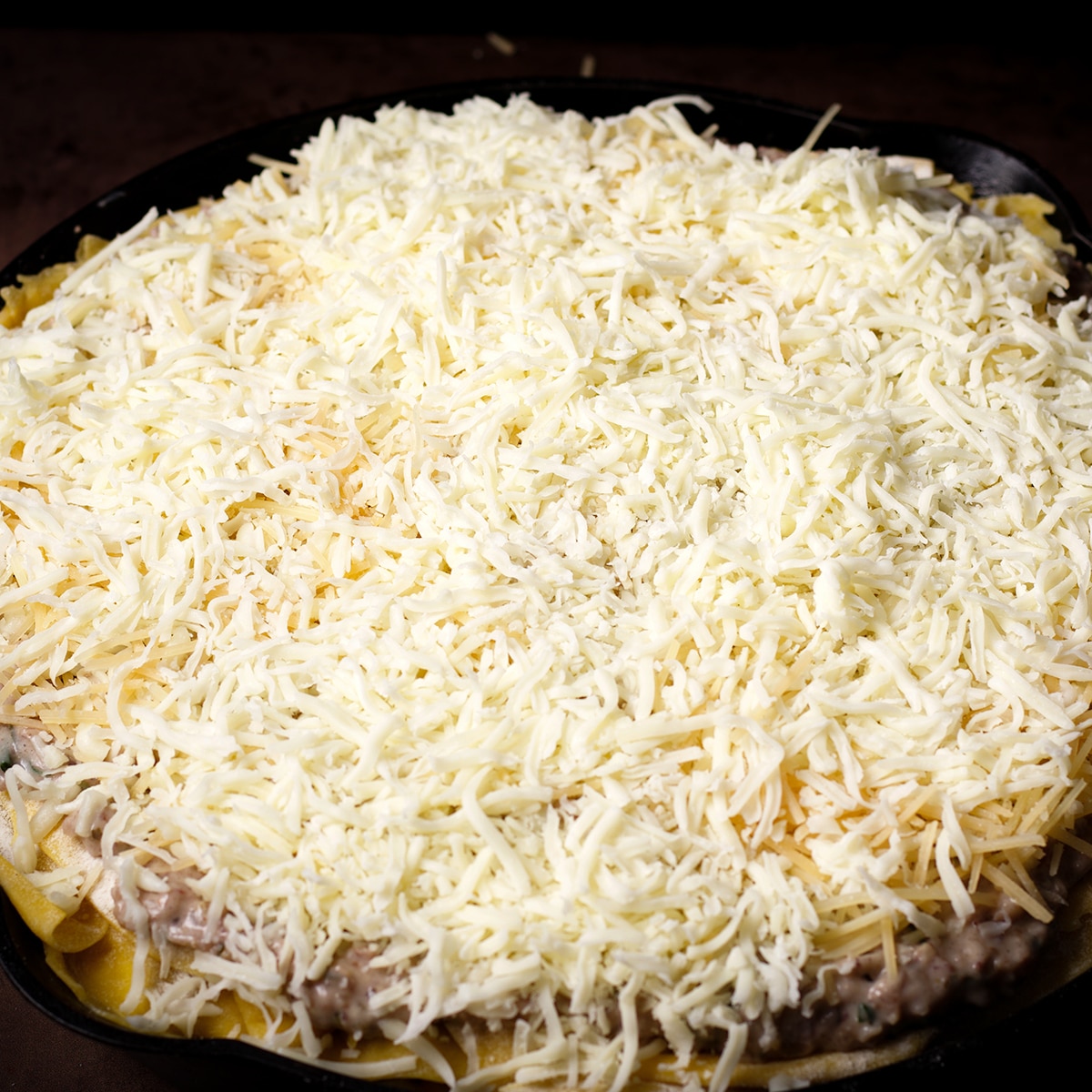 A skillet vegetable lasagna with white sauce that's ready to bake.