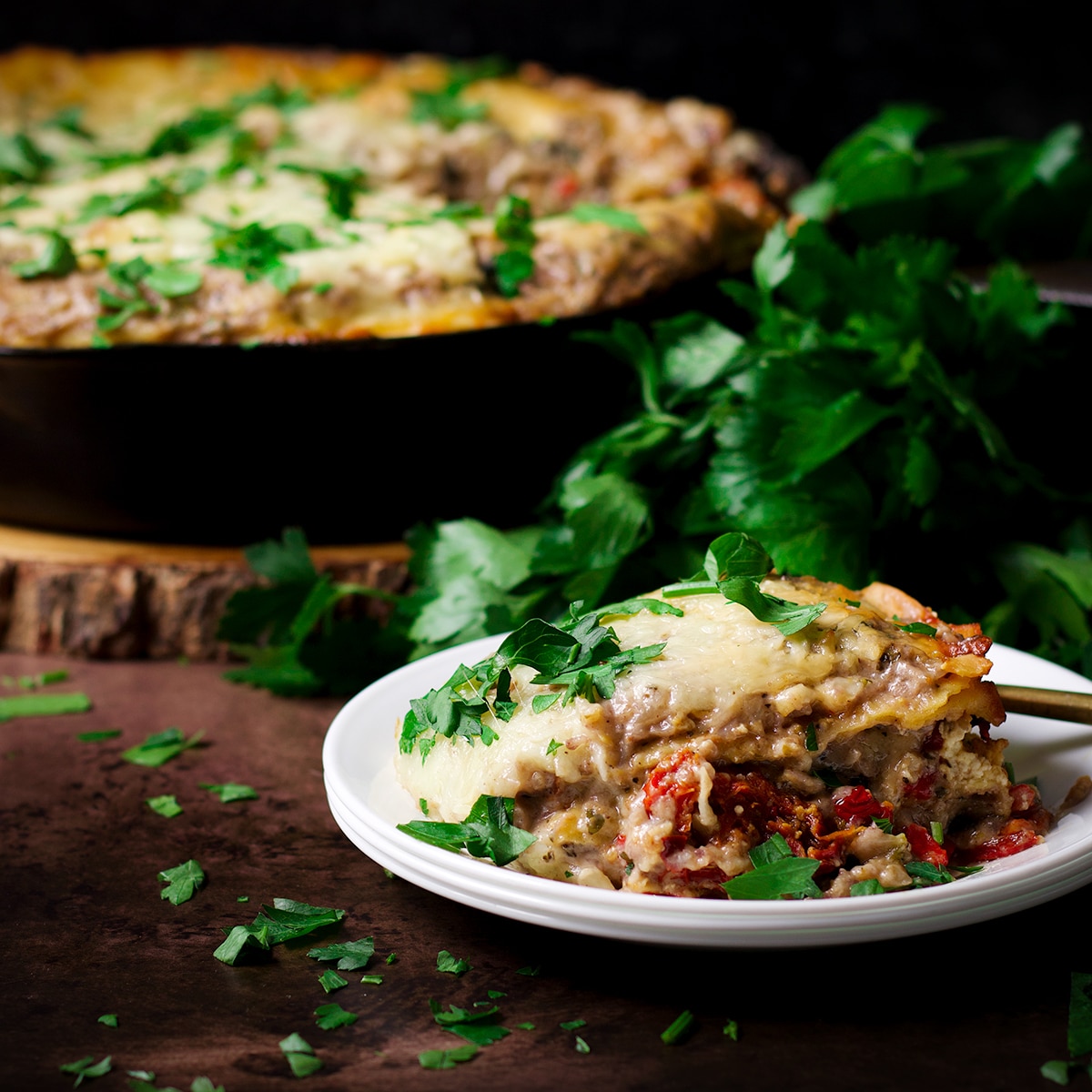A plate of vegetarian lasagna resting on a table next to skillet baked vegetable lasagna.
